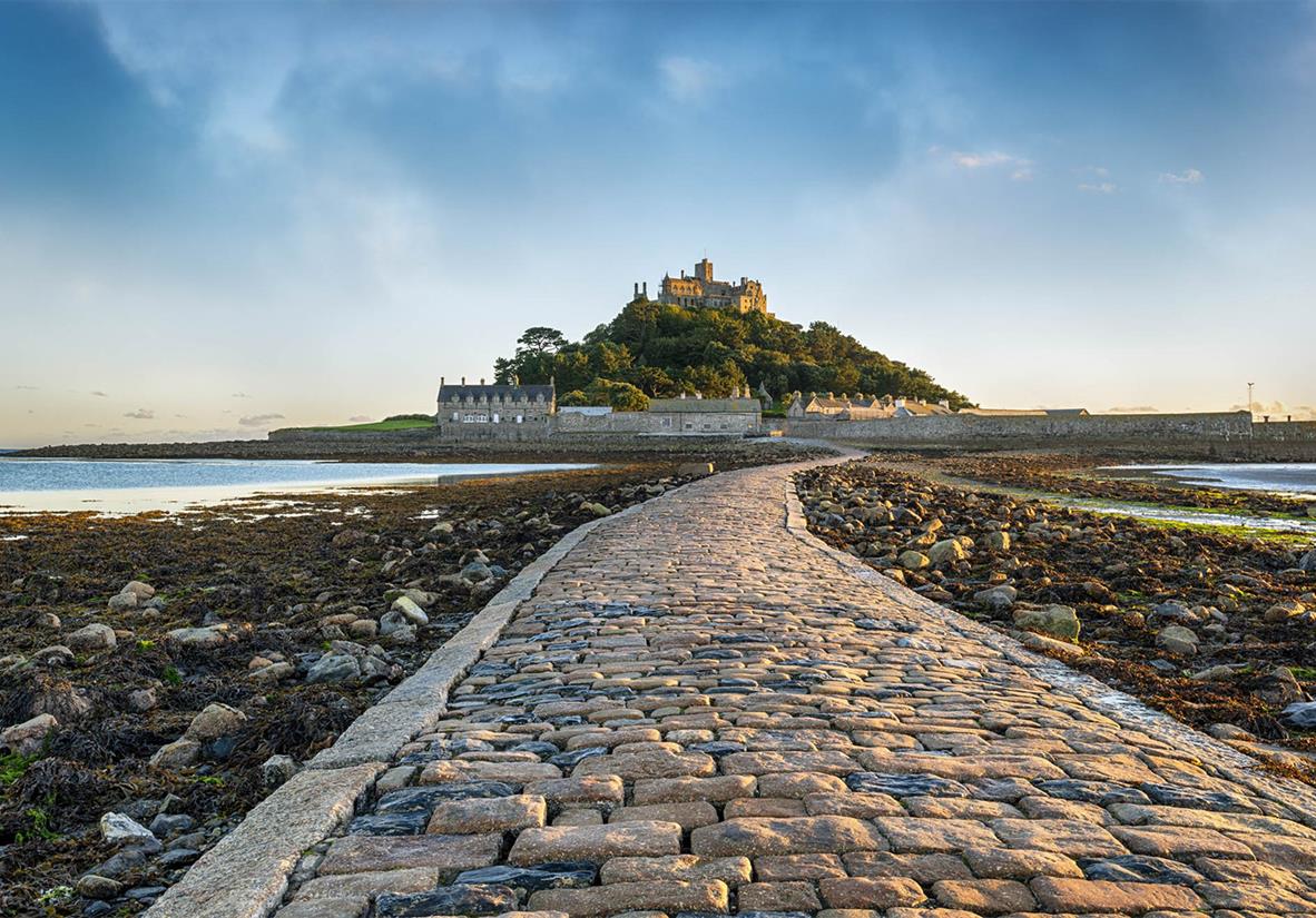 Cobbled causeway leading to St Michael’s Mount in Cornwall, a tidal island with a historic castle and buildings surrounded by sea and rocky shore.